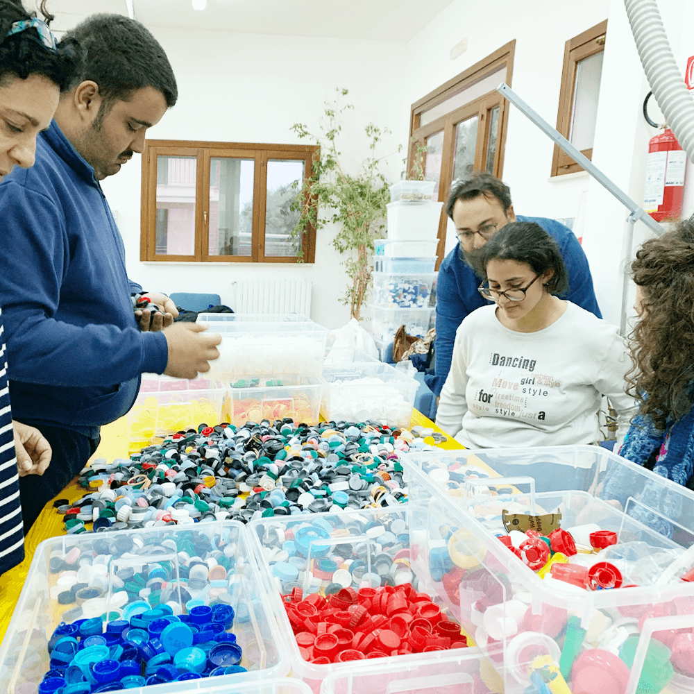 Tre ragazzi e due ragazze che smistano tappi rossi blu e di colori vari