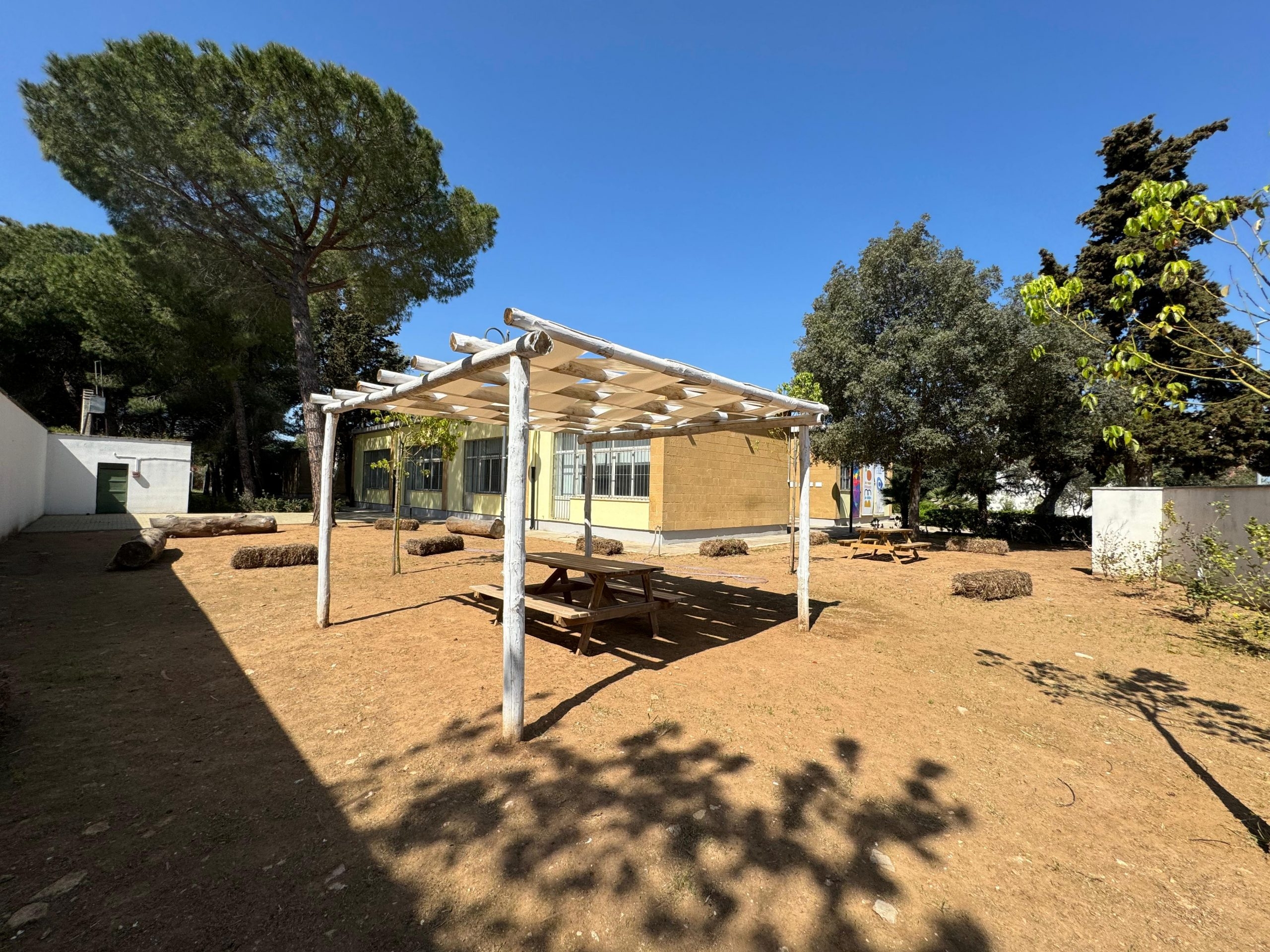 scorcio con alberi, panca e tavolo sotto un gazebo nel giardino della biblioteca comunale Bibliò sede del Nodo Galattica di Trepuzzi