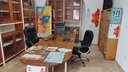Una stanza con una scrivania con un laptop, delle sedie nere e poster con la scritta 'Galattica' sulle pareti