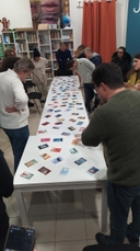 Gruppo dei partecipanti intorno al tavolo sul quale sono state disposte le carte del gioco Dixit. L'attività è fatta in occasione del laboratorio "Statt Citt - Diamo voce ai giovani" presso il Nodo Galattica di Cisternino, 15 gennaio 2024