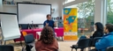 Persone sedute su sedie in una stanza davanti a una presentazione sul proiettore, con un docente che presenta