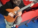 Ragazza con una maglia nera suona una chitarra classica di legno poggiata su poltrone rosse.