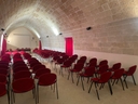 Nodo "Galattica" a Castrì. Una grande sala con sedie rosse e una parete di pietra.