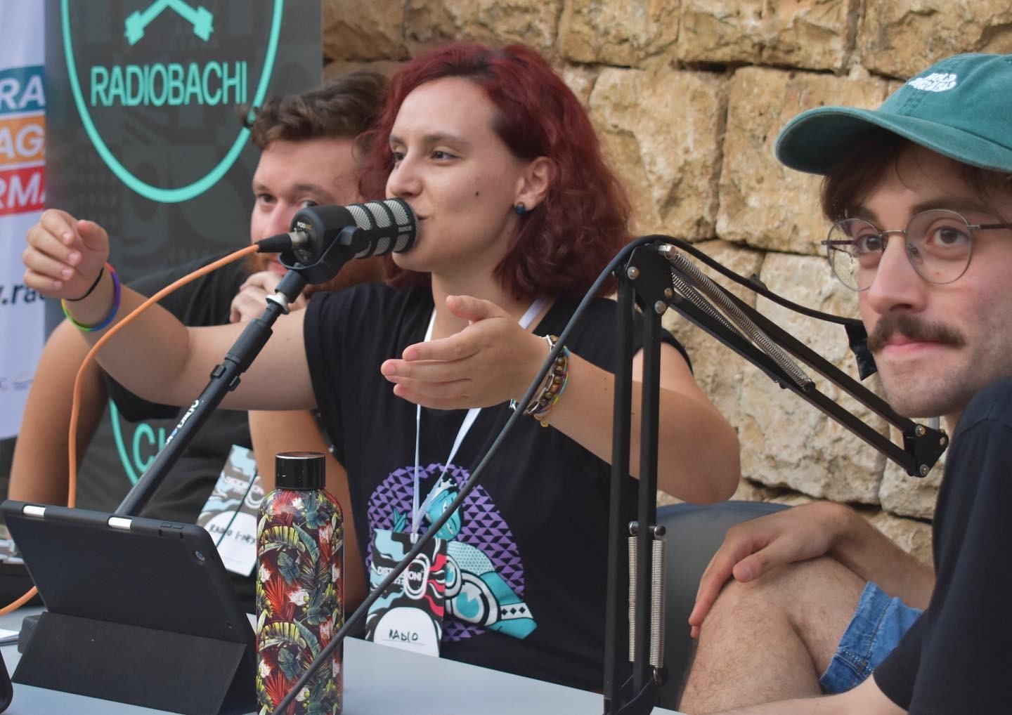 L'immagine ritrae due ragazzi e una ragazza, tutti e tre speaker di Radio Bachi: la ragazza al centro della foto sta parlando al microfono, mentre gli altri due guardano fuori campo.