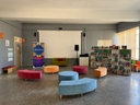 Ampia sala con divanetti colorati, telo di proiezione e scaffali con libri all'interno della Biblioteca di Comunità Bibliò