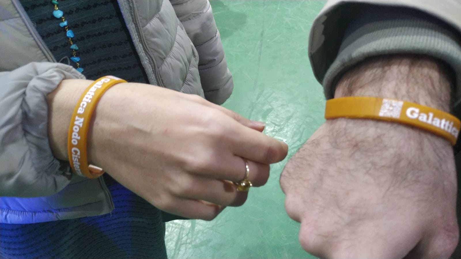 Primo piano dei gadget di Galattica, due braccialetti in plastica con la scritta "Galattica" sul polso di due persone presenti all'evento di Inaugurazione del Nodo Galattica di Cisternino, 18 novembre 2023