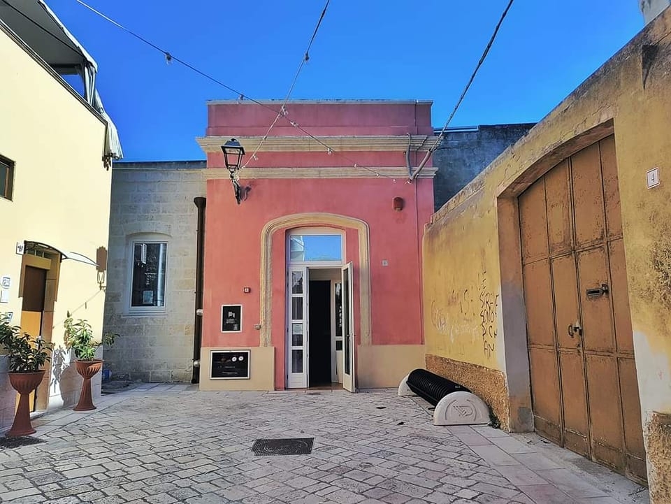 Vicolo che arriva a una porta bianca che si apre su uno facciata rosa