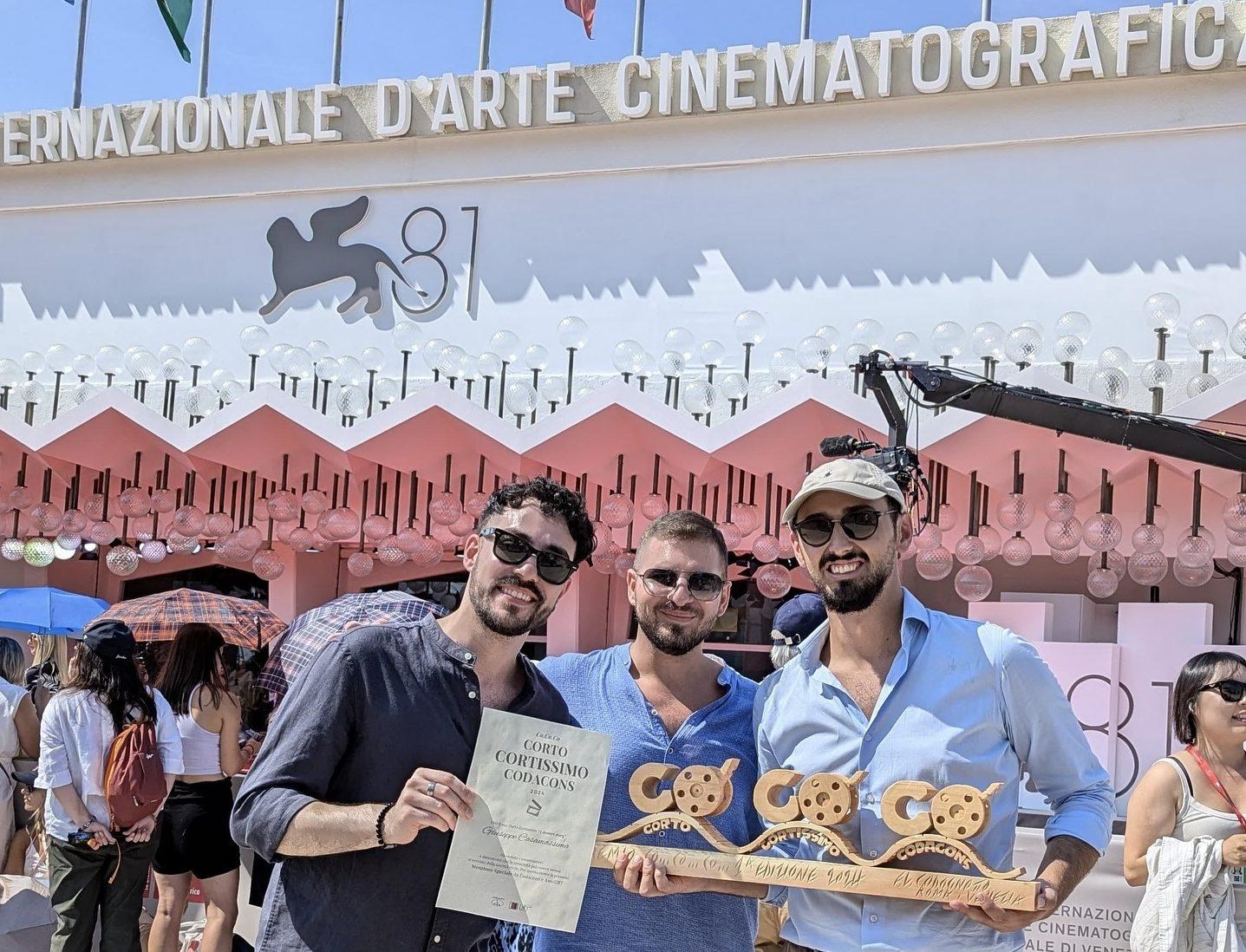 Tre giovani sorridenti tengono in mano un premio, orgogliosi del loro riconoscimento al Festival del Cinema di Venezia