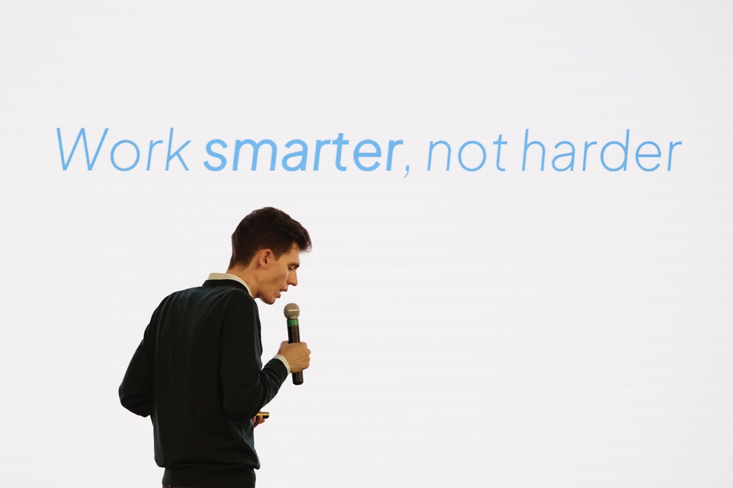 Mario De Pinto mentre tiene un discorso con la frase 'Work smarter, not harder' proiettata sullo sfondo