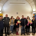 momentodel laboratorio radici future sette persone in piedi davanti a un tavolo sorridenti. Una ragazza e una signora tengono in mano un mazzo di fiori ciascuno