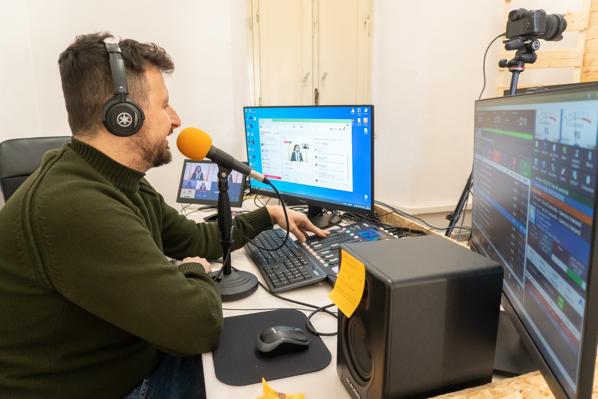 Immagine di un uomo con un maglione verde seduto di fronte a due monitor