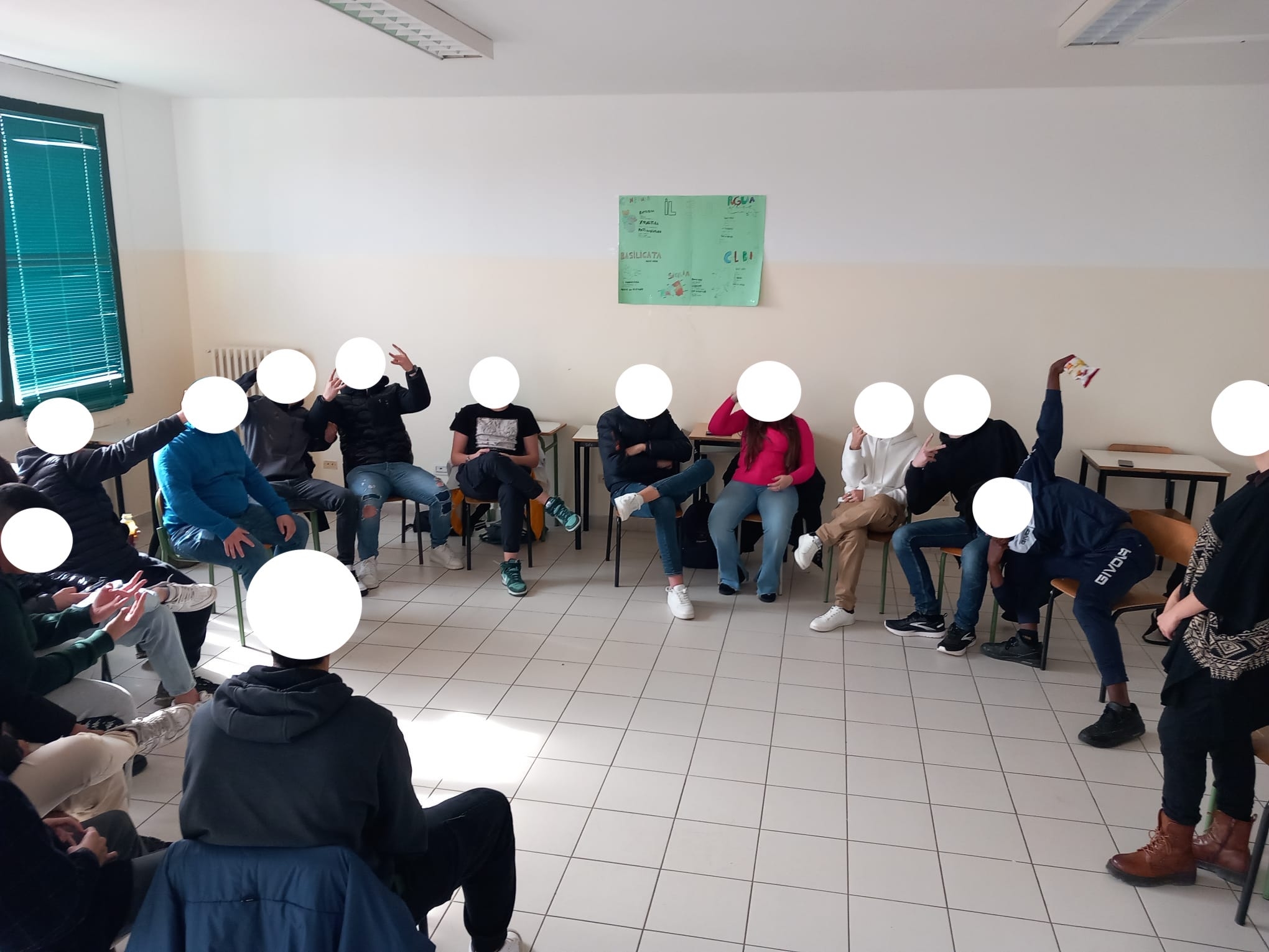 studenti in cerchio seduti su delle sedie. A destra donna in piedi