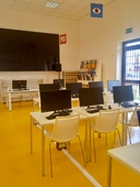 Aula pc della sede del nodo di San Pancrazio Salentino Sedie e tavoli bianchi con pc neri, in fondo un grande schermo nero.