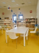 Sala studio della sede del nodo di San Pancrazio Salentino Sedie bianche attorno a tavolo bianco e in fondo due scaffali e sullo sfondo due finestre sul muro bianco.