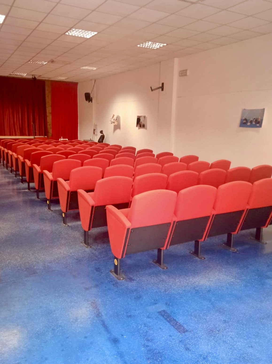 Teatro con file di poltrone rosse e il palco con sipario rosso sullo sfondo.