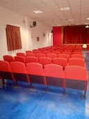 Teatro della sede del nodo di San Pancrazio Salentino Teatro con file di poltrone rosse e il palco con sipario rosso sullo sfondo.