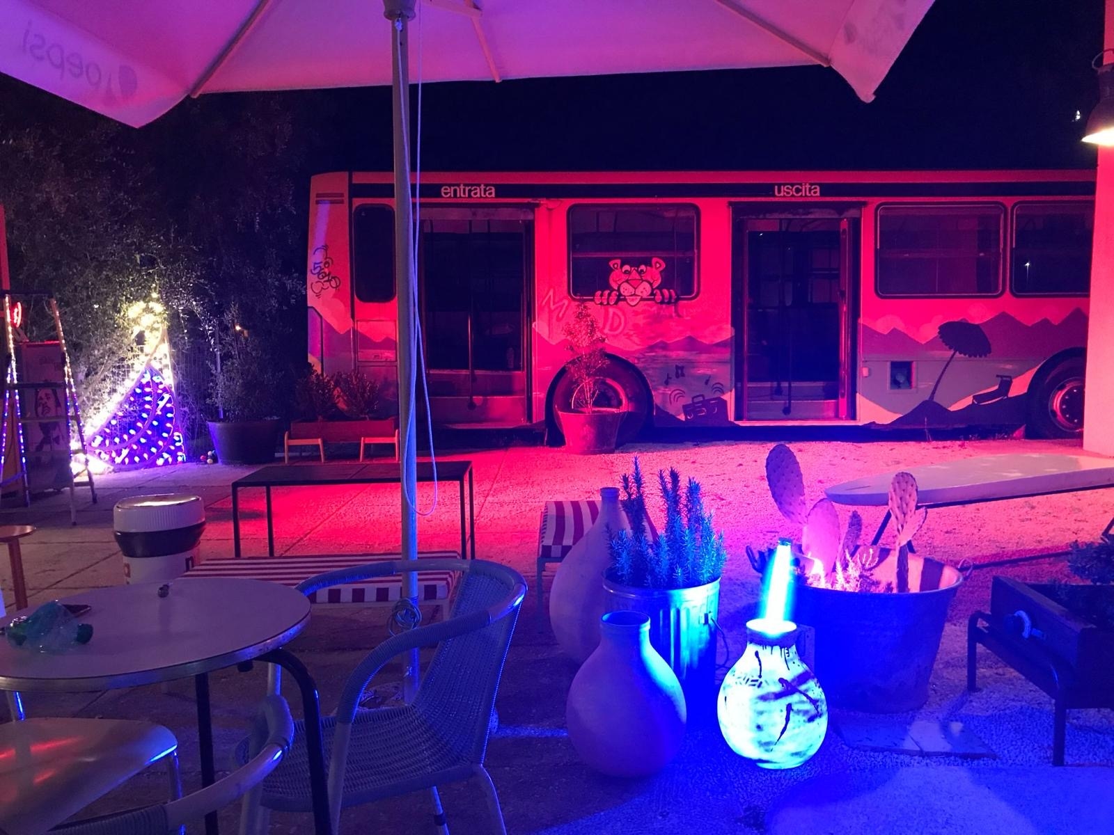 Spazio esterno con tavolini e un vecchio scuolabus riadattato a spazio di coworking
