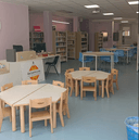 interno vuoto 3 Panoramica della sala adiacente alla vetrata : presenta sulla sinistra la postazione dell'operatore e alla base di essa è presente un pannello col logo del progetto Galattica. Di fronte sono presenti 2 tavolini per bambini e una schiera di tavoli per adulti. Sulla sinistra, dietro la postazione dell'operatore è presente un serie di scaffali