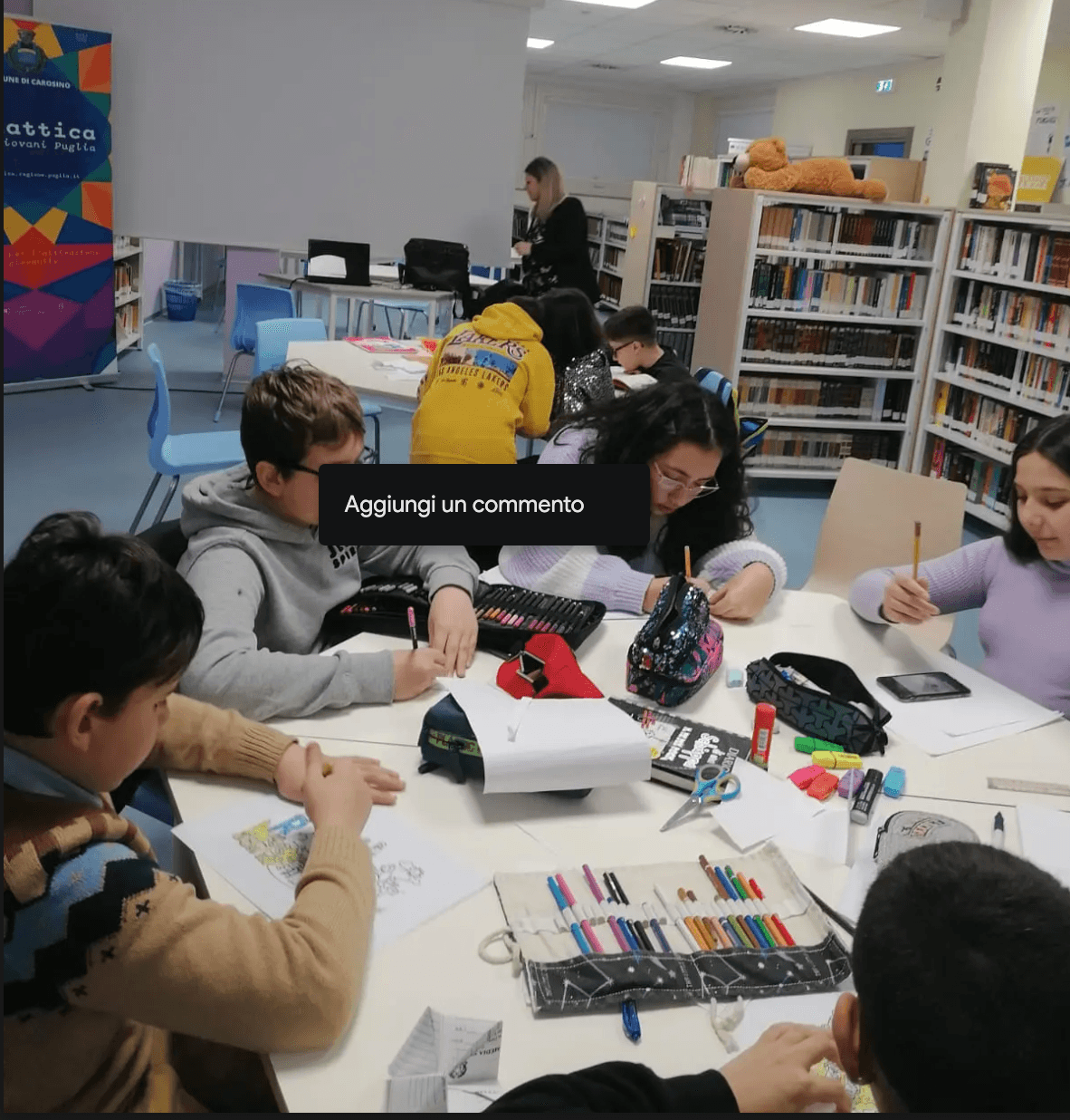 I ragazzi sono impegnati nella loro attività seguiti da un coordinatore posto sullo sfondo tra gli scaffali ed il pannello del videoproiettore.