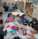 Nella foto sono presenti dei bambini seduti sulle sedioline mentre sono impegnati nell'attività di disegno. I bambini sono acompagnati dai genitori posti alle loro spalle sul tavolo più grande circondati dgli scaffali. Nella foto sono presenti dei bambini seduti sulle sedioline mentre sono impegnati nell'attività di disegno. I bambini sono acompagnati dai genitori posti alle loro spalle sul tavolo più grande circondati dgli scaffali.