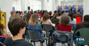 4. Presentazione del progetto
4. Sala spaziosa costituita da molteplici colonne e diverse sedute. Nella foto è presente un ampio pubblico che ascolta la presentazione del progetto.