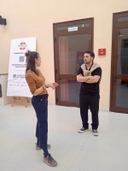 Laboratorio del Piano Regionale "Think Europe" al nodo San Pancrazio Salentino Una ragazza e un ragazzo parlano davanti a una porta dello spazio del nodo accanto alla quale c'è il roll up di Galattica.