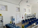 Sala dell'incontro "8 marzo Start Progetto Galattica" Sala con a sinistra un tavolo blu con brochure e vasi con fiori gialli, di fronte e sulla destra poltrone blu con un tappeto blu nel mezzo, in fondo scaffali bianchi sulle mura bianche.