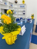 Sala convegni della sede del nodo di Melendugno Tavolo blu con vaso di fiori gialli, bottiglie d'acqua e scaffali bianchi sullo sfondo