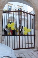 Entrata della sede del nodo di Melendugno Cancello nero all'interno di un arco con dei fiori gialli sulle inferriate.