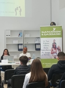 Incontro "La verità sulle droghe" Giovani seduti, visti di spalle, che si trovano di fronte a due persone sedute dietro a un tavolo bianco con un pc e accanto un roll up.