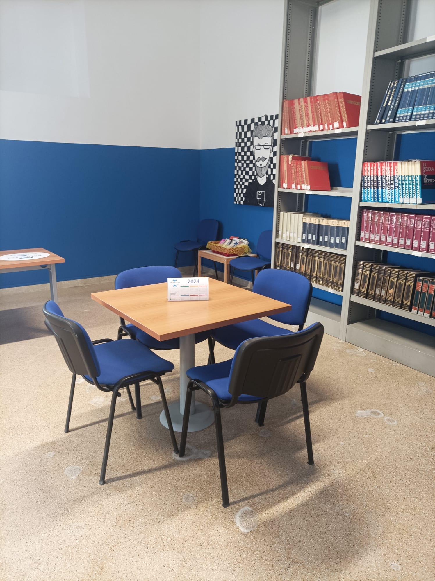 Sala con tavolo quadrato in legno e quattro sedie blu e una libreria sullo sfondo.