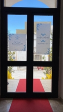 Uscita del nodo di Melendugno Vista interna di una porta a vetri con tappeto rosso che porta alle scale esterne del nodo di Melendugno.