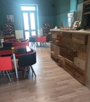 Bar all'interno del nodo di Melendugno Bar con bancone in legno composto da cassetti, tavoli e sedie rosse, parquet e sullo sfondo una porta a vetri in un muro verde.