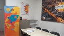 spazio interno nodo di Taviano stanza con tavolo e tre sedie. Al muro un grande poster con una foto della città illuminata di Taviano e sopra il logo di Galattica. Sulla parete del muro adiacente sulla sinistra, altro poster con logo di Galattica e davanti al tavolo roll-up di Galattica.