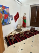 La stanza principale al primo piano. Stanza ampia con pavimento chiaro e lucido, mura bianca e porta in legno. Al muro tessuti colorati e manichino con abiti tradizionali.