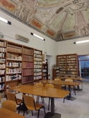 la biblioteca spazio della biblioteca composto da tavoli con sedie al centro della stanza, scaffali con libri alle pareti, soffitto affrescato