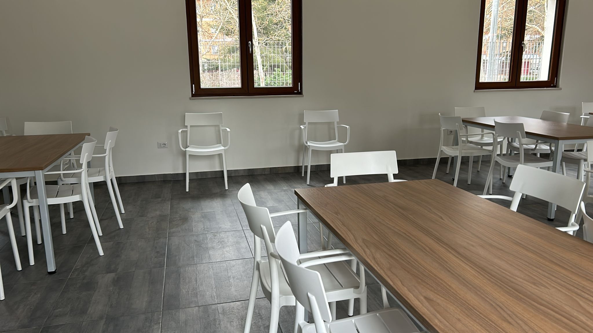 Stanza con pavimento scuro, mura bianche, finestra, tavolo in legno e sedie bianche