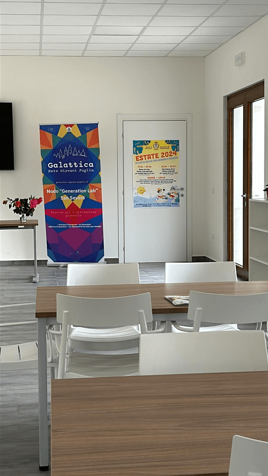Tavolo in legno in primo piano con sedie bianche e sullo sfondo roll-up su sfondo blu di Galattica