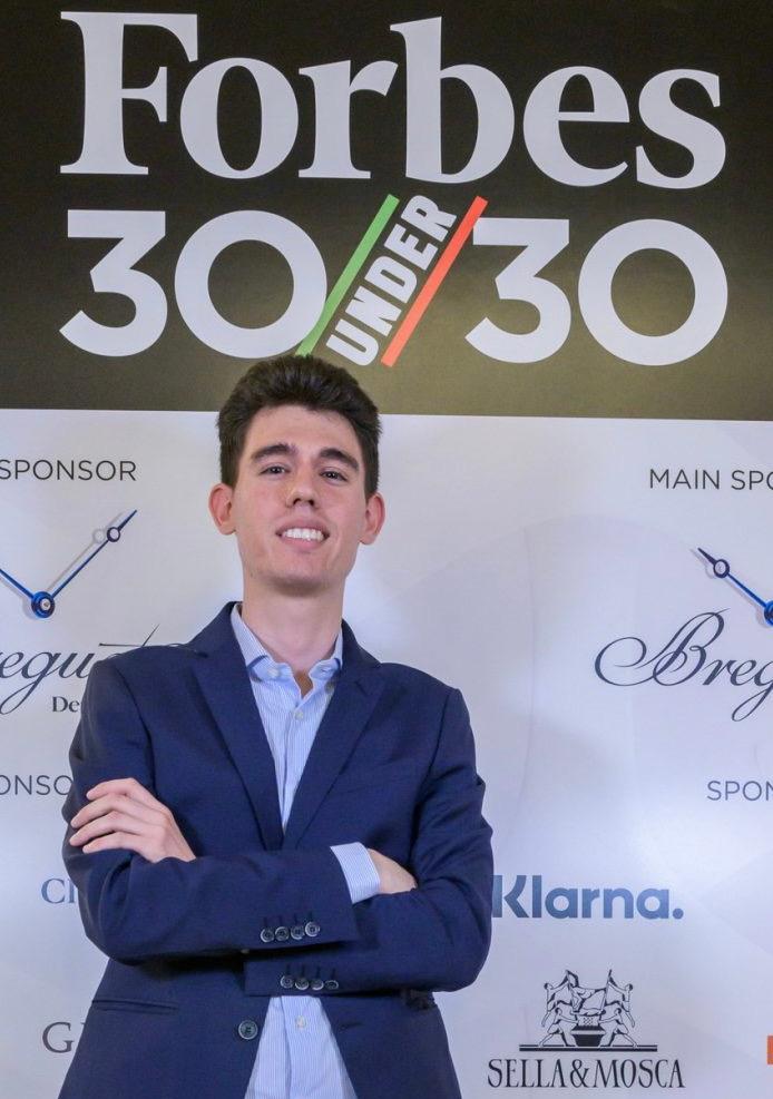 Mario De Pinto, premiato da Forbes 30 Under 30, in posa davanti al logo ufficiale dell'evento