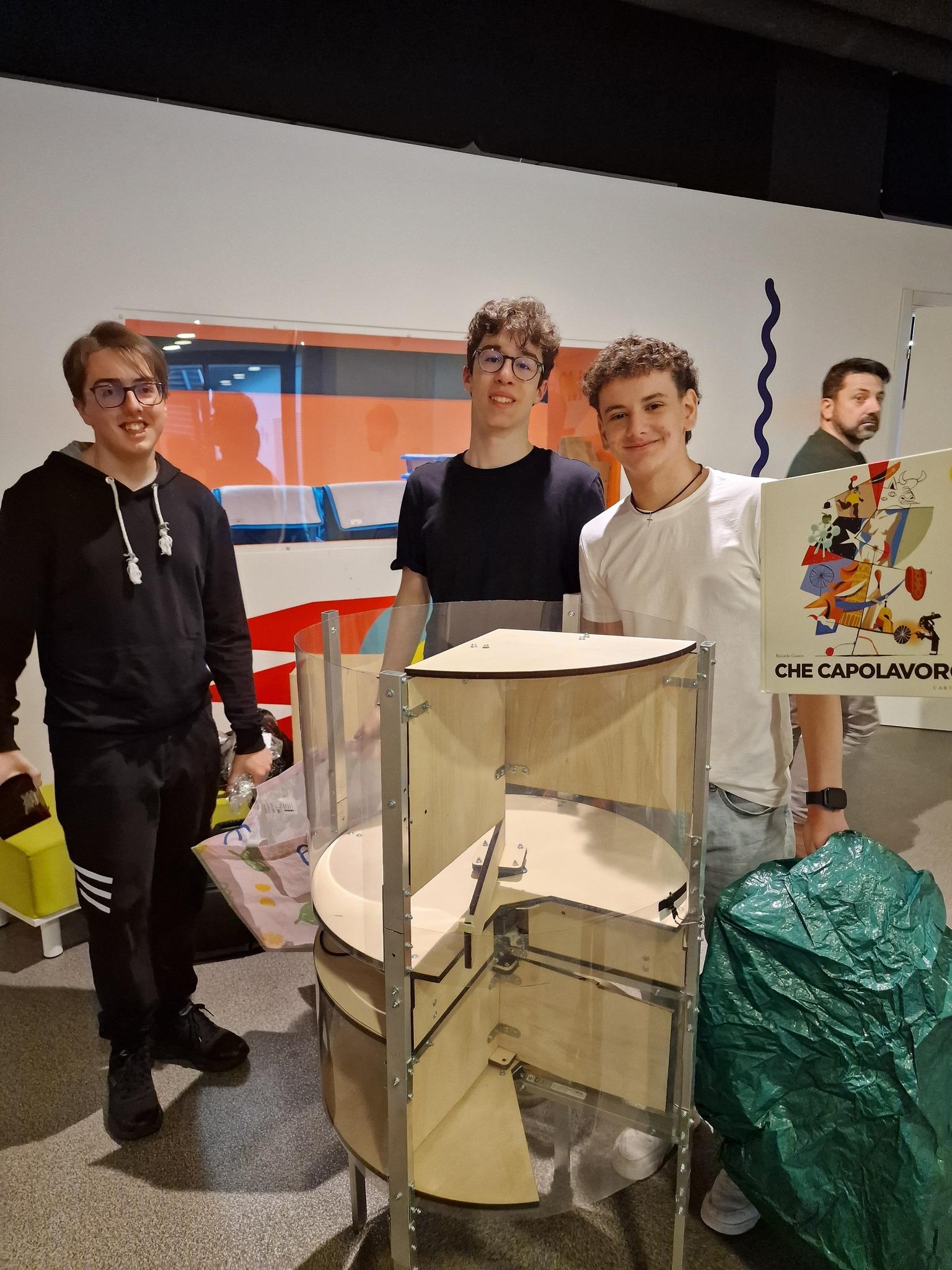 Tre membri del Team Remate posano accanto al prototipo del cestino intelligente durante un evento espositivo