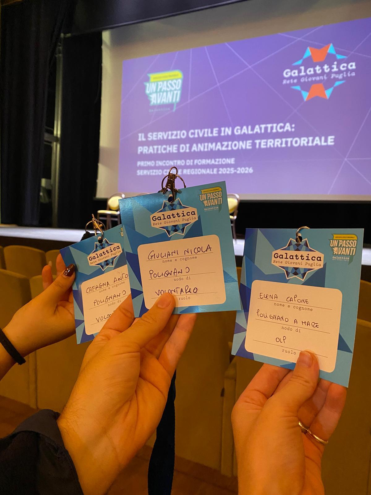 Primo incontro di formazione del Servizio Civile regionale.
I volontari e gli operatori locali di progetto del Nodo di Polignano a Mare partecipano con entusiasmo al percorso del Servizio Civile Regionale 2025–2026, promosso da Galattica – Rete Giovani Puglia. Nella foto si vedono tre persone che tengono in mano dei badge di riconoscimento blu con il logo di “Galattica – Rete Giovani Puglia”. I badge riportano i nomi e i ruoli dei partecipanti a un incontro di formazione. Sullo sfondo, si vede un grande schermo con una proiezione che riporta il titolo dell’evento: “Il Servizio Civile in Galattica: pratiche di animazione territoriale – primo incontro di formazione del Servizio Civile Regionale 2025–2026”. La scena si svolge in una sala conferenze con sedie disposte di fronte al palco. L’atmosfera è quella di un momento di formazione e partecipazione giovanile.